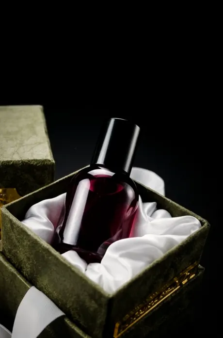 زجاجة عطر داكنة على حرير أبيض داخل صندوق هدية مخملي