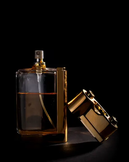 زجاجة عطر بغطاء ذهبي مفتوح على خلفية داكنة